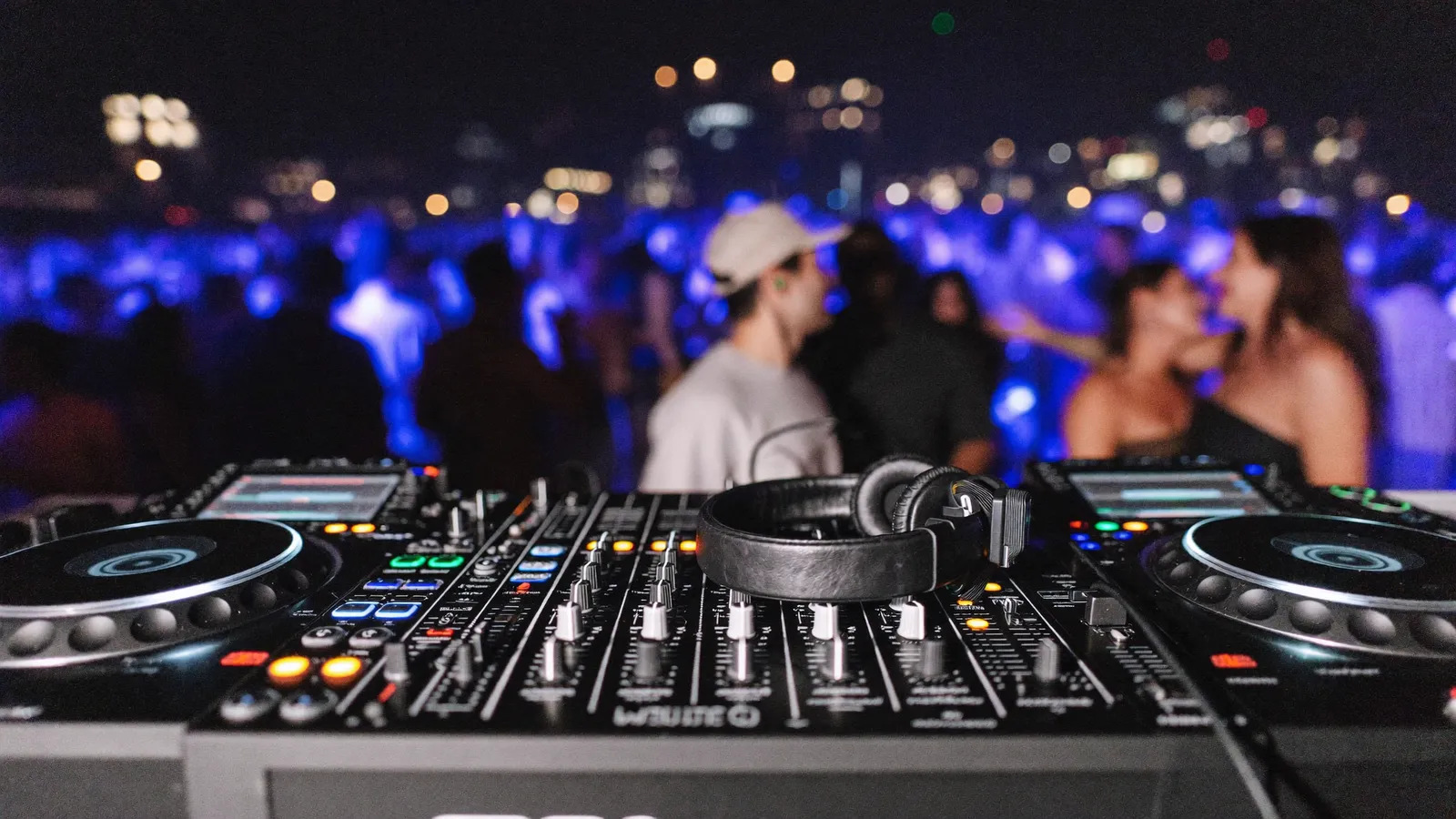 DJ-Pult mit Kopfhörern und farbigem Partylicht, Tanzfläche im Hintergrund