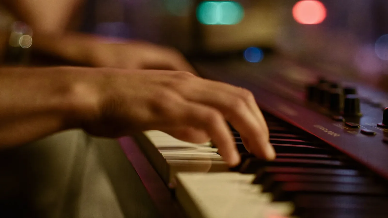 Hände auf den Tasten eines Keyboards, farbiges Bühnenlicht im Hintergrund